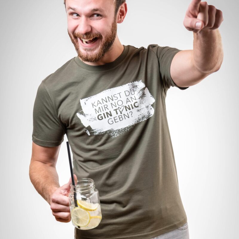 Mann mit T-Shirt und einem Gin-Tonic in der Hand. Auf dem Shirt steht "Kannst du mir bitte no an Gin Tonic gebn!"